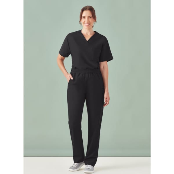 A woman wearing black unisex straight leg scrub pants with a short-sleeve top, standing against a light background.