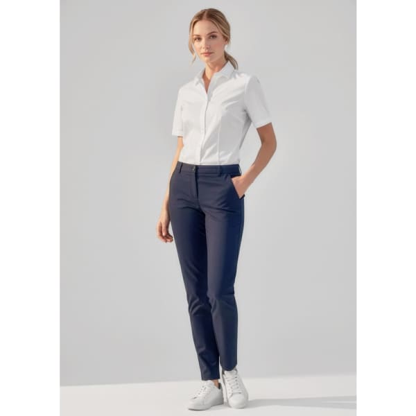 A woman is wearing navy slim leg pants with a white short-sleeve shirt and white sneakers, standing with hands in pockets.