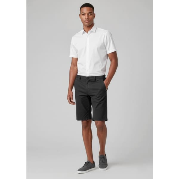 A man wearing black cargo shorts with a white short-sleeved shirt and grey shoes, standing against a neutral background.