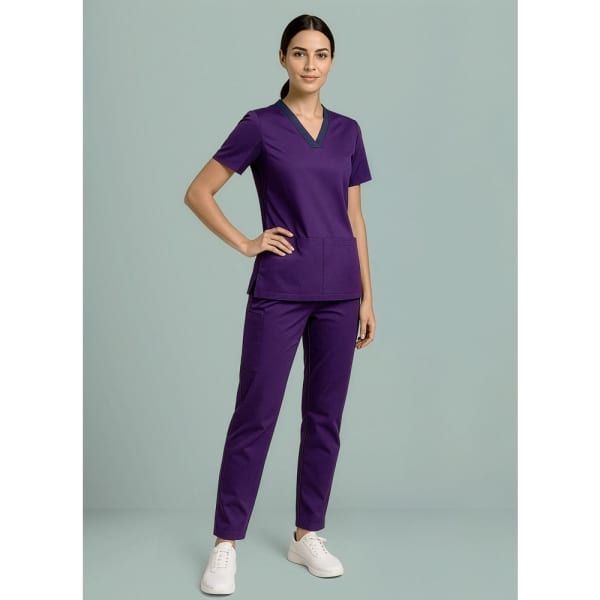A model wearing purple women's scrub top and straight leg scrub pants, paired with white sneakers.