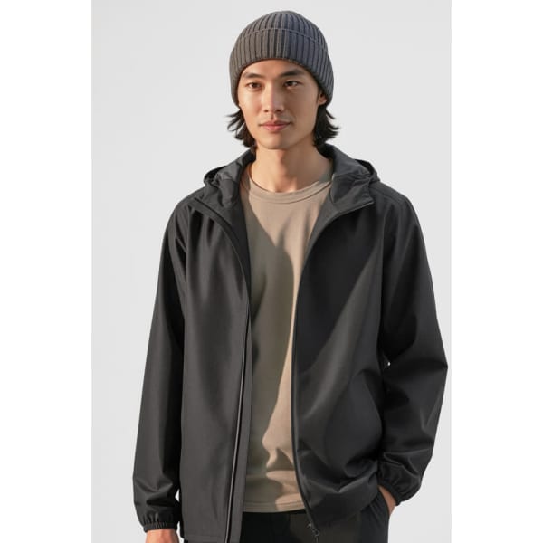 A man wearing a black rain jacket and a grey beanie, standing against a light background. The jacket has a logo.