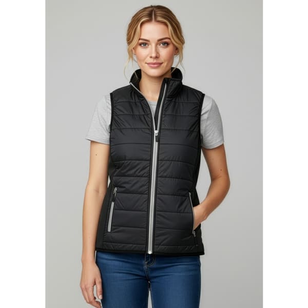 A woman is wearing a black puffer vest with a zip front, paired with a grey t-shirt and blue jeans.