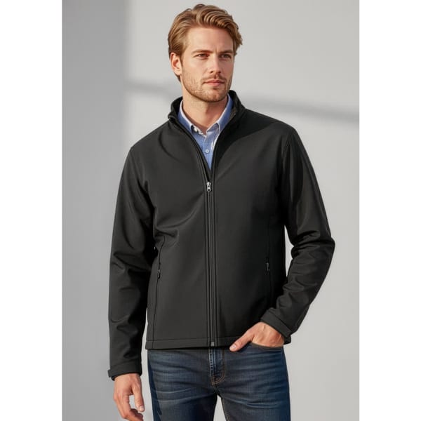 A man wearing a black soft shell jacket, standing against a light background, featuring a branding logo on the jacket.