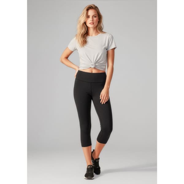 A model wearing black 3/4 leggings paired with a grey knotted t-shirt and black sneakers, featuring a logo.
