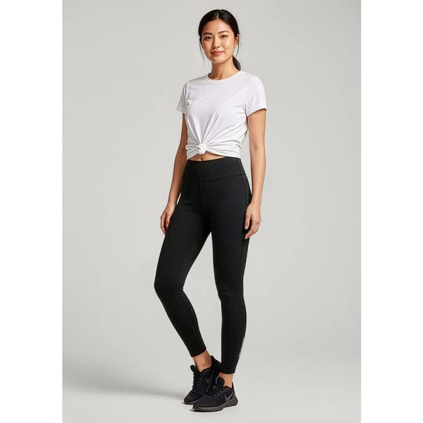 A woman stands wearing black leggings and a white t-shirt, featuring a logo on the leggings.