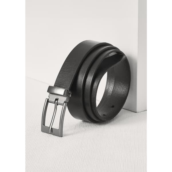 A black leather belt is displayed with a sleek silver buckle, leaning against a white surface.