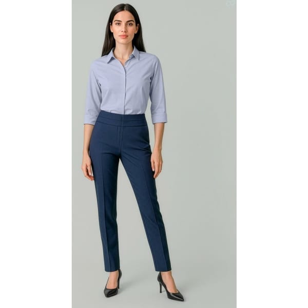 A woman stands in navy slim leg pants paired with a light blue shirt, featuring a logo on the clothing.