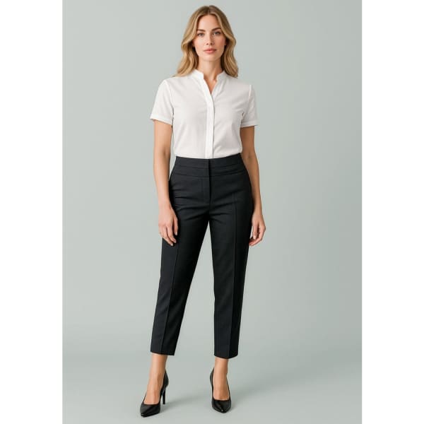 A woman stands wearing slim leg pants in black, paired with a white button-up shirt and high heels.
