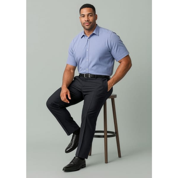 A man wearing a light blue shirt and navy straight-leg slacks, seated on a wooden stool. The slacks feature an adjustable waist.