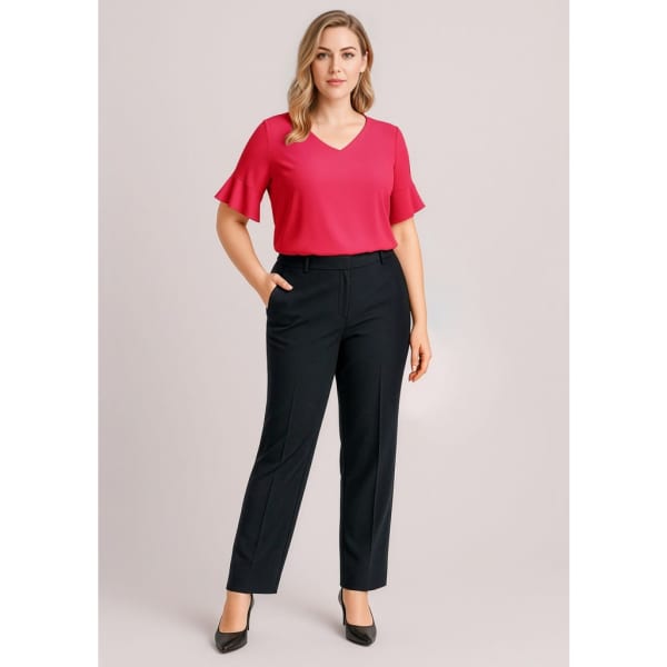 A woman wears a pink top and navy slacks, standing with one hand in her pocket. The pants have a logo.