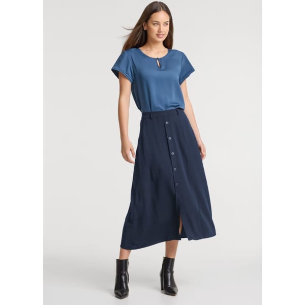 A model wearing a navy blue midi skirt with buttons and a matching blue top, paired with black ankle boots.