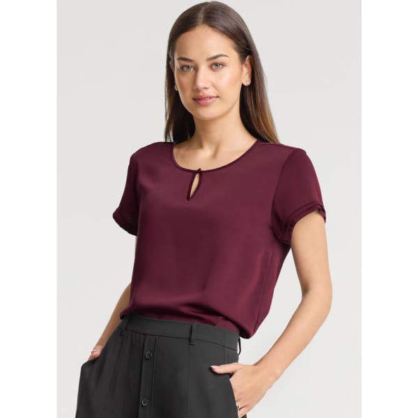 A burgundy short sleeve blouse with a keyhole detail, paired with black trousers and featuring a logo.