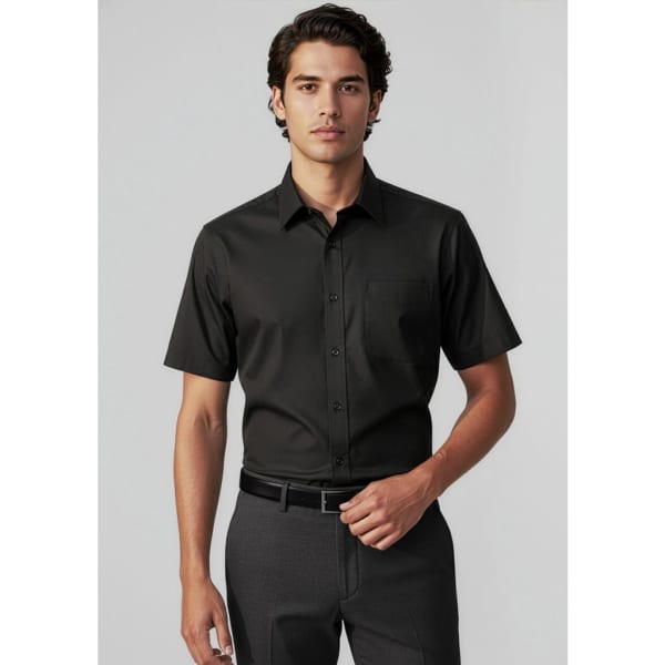 A black short sleeve button-up shirt with a chest pocket, worn with grey trousers. The model is standing straight.