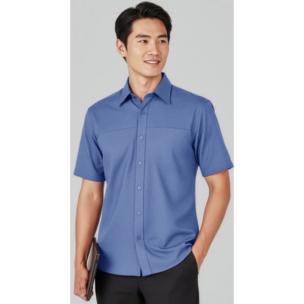 A short sleeve button-up shirt in blue, featuring a front pocket and a logo. Model holds a tablet and smiles.