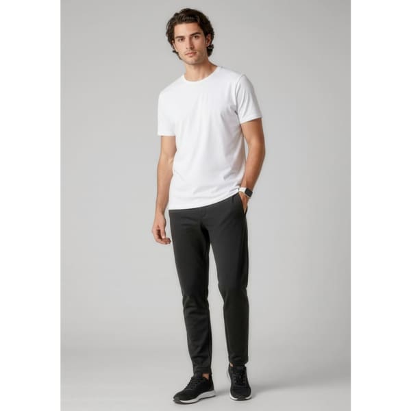 A man is wearing black track pants and a white t-shirt, paired with black sneakers. The pants have a logo.