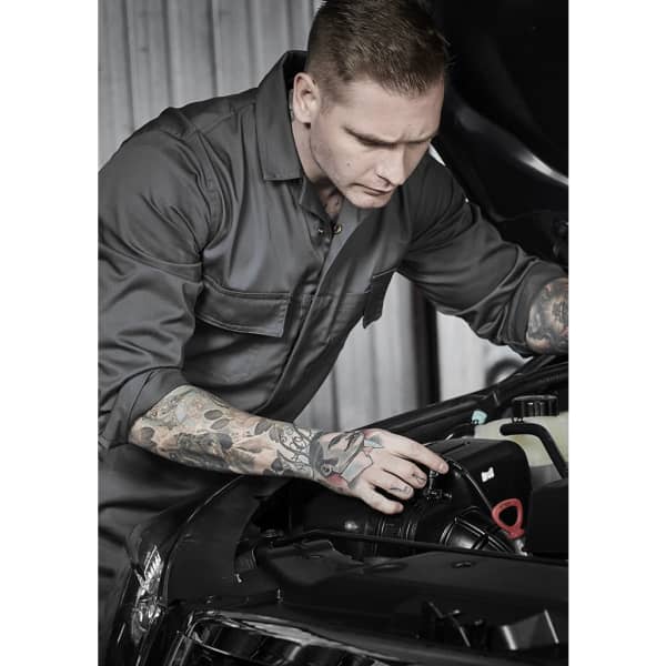 A man wearing a grey service overall works on a car engine, showcasing his tattoos. The image focuses on the overall's design.