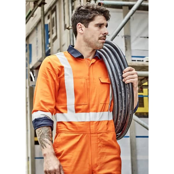 A man in an orange cotton overall with reflective stripes, holding black cables, set against a construction backdrop.