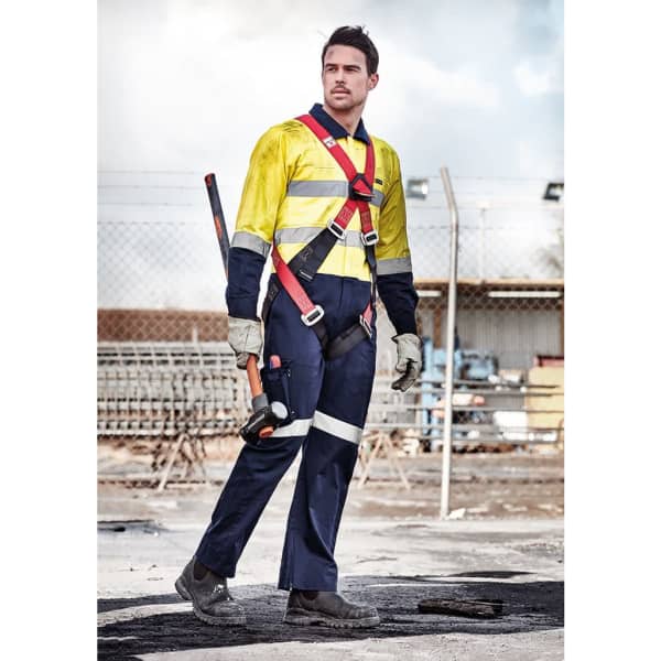 A man in a high-visibility yellow and navy overall wears a harness with gloves and a tool, set against an industrial background.