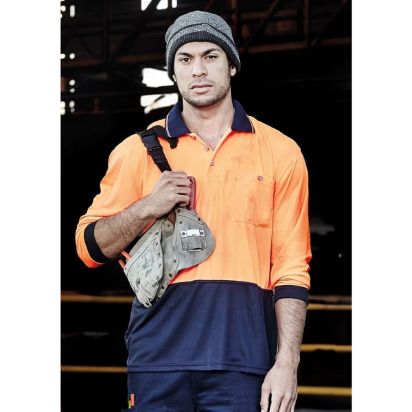 A man wearing an orange and navy blue long sleeve polo shirt, holding a work bag and wearing a grey beanie.