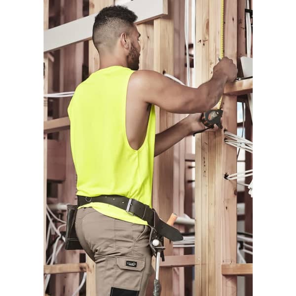A man wearing a high visibility sleeveless tee in fluorescent yellow, working on wooden framing with tools.