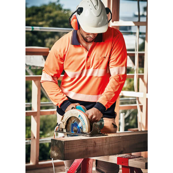 A worker in an orange segmented tape long sleeve polo shirt operates a circular saw at a construction site.