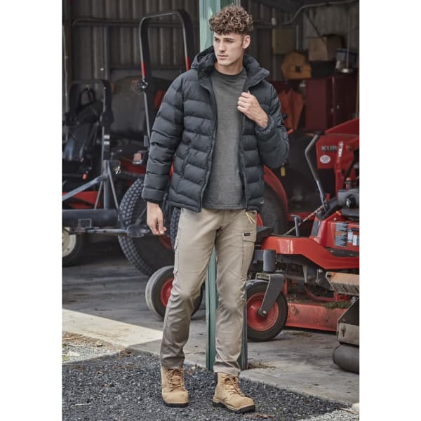 A black hooded puffer jacket is worn over a grey shirt, paired with beige pants and tan boots in an outdoor setting.