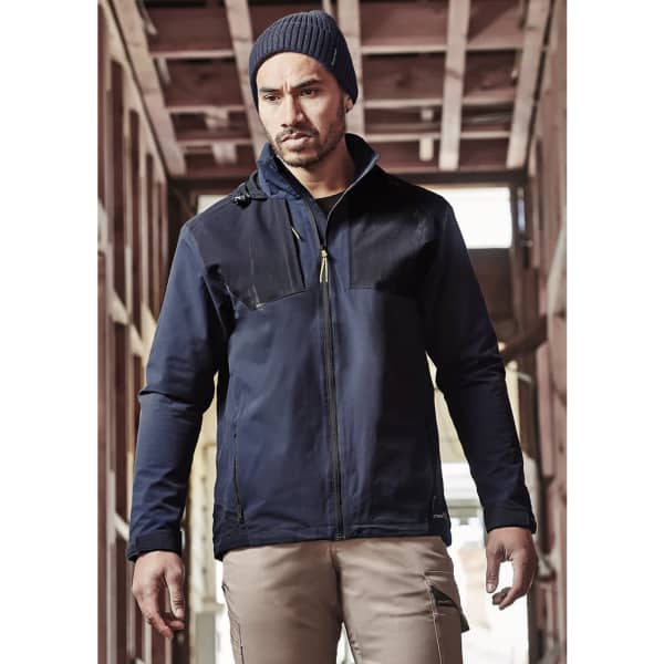 A navy blue waterproof jacket features a logo and is designed for unisex wear, shown in a rustic setting.