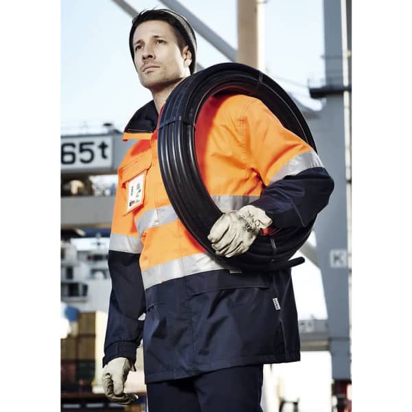 A man in an orange and navy waterproof jacket holds a coil of cable, wearing gloves and a beanie.
