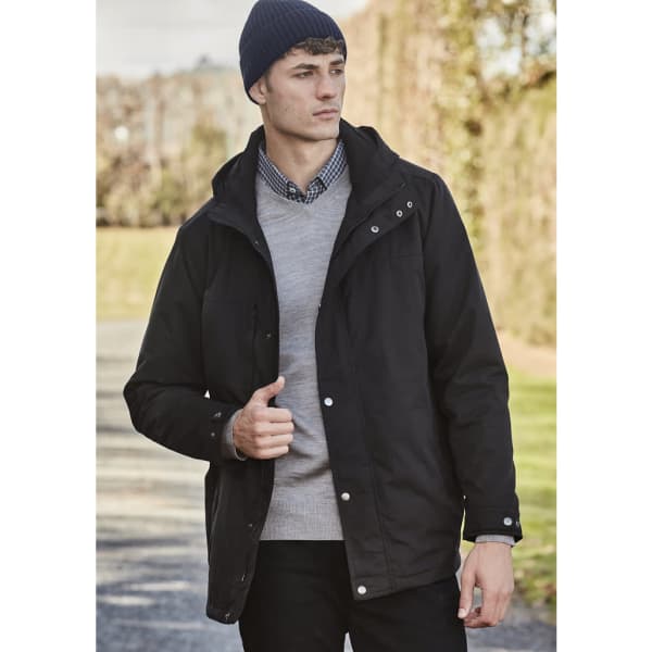 A model wearing a black jacket and a navy beanie, standing outdoors with greenery in the background.