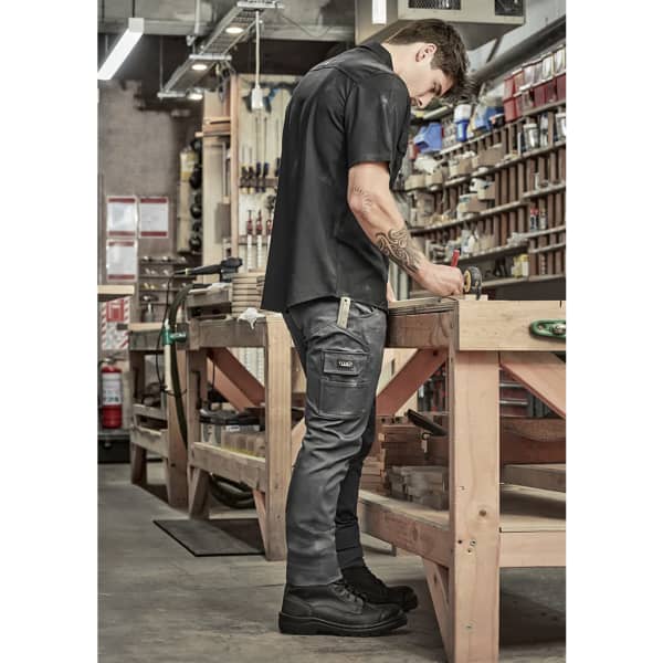 Mens essential basic stretch cargo pants in dark grey, featuring pockets, worn by a man in a workshop setting.