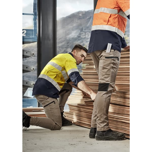 Men wearing workwear, one in a yellow and navy shirt and the other in an orange shirt, with cuffed beige stretch pants.