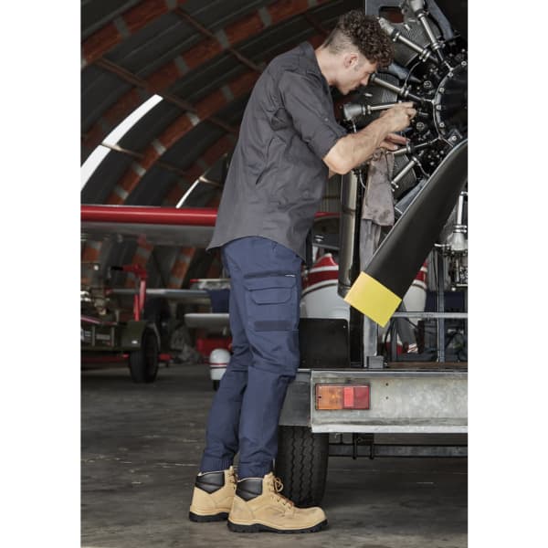 Mens Streetworx Heritage Pant in navy, paired with tan work boots, worn by a man repairing machinery in a hangar.