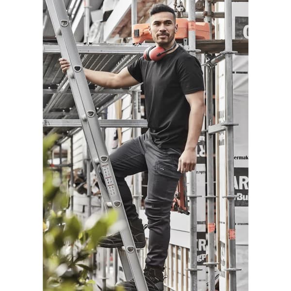 A man wearing black Men Streetworx Comfort Pants and a black T-shirt, standing on a ladder at a construction site.