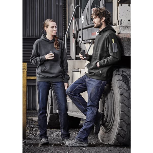 A pair of adults wearing black hoodies and blue stretch denim work jeans, standing beside a large vehicle.