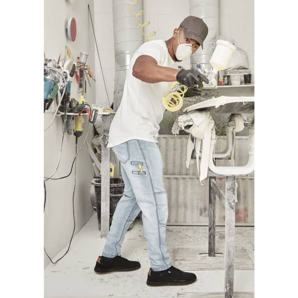 A man wearing light blue stretch jeans and a white t-shirt is spray painting in a workshop.