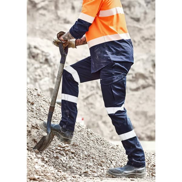 A person wearing orange and navy cargo pants with white stripes, using a shovel on rocky terrain.