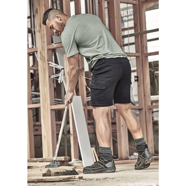 A man in a green t-shirt and black shorts is cleaning a construction site. He is wearing work boots and socks.