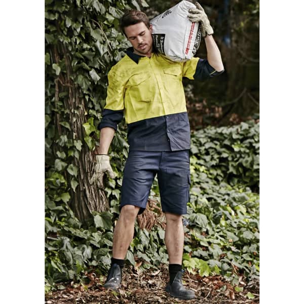 Men's rugged cooling vented shorts in navy, paired with a yellow work shirt, set against a lush green background.