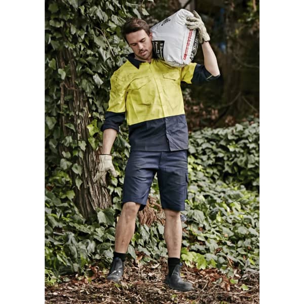 Men's rugged cooling vented shorts in navy, styled with a bright yellow shirt, set against a leafy background.
