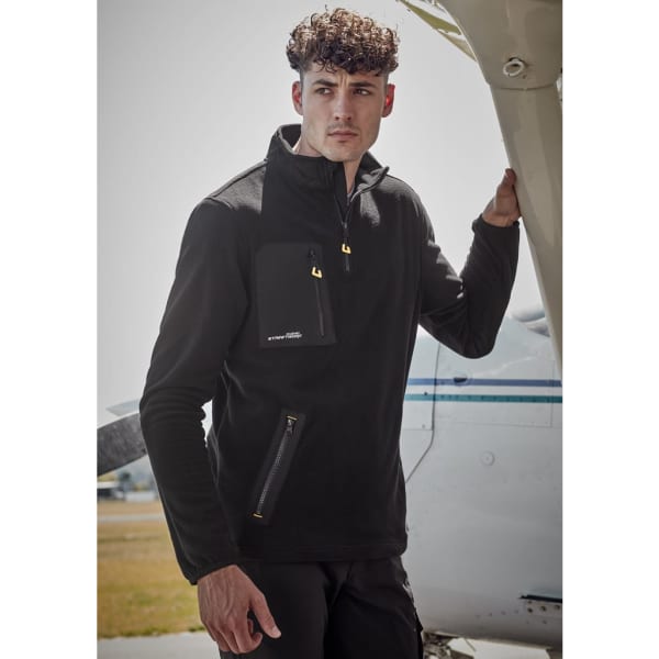 A model wearing a black unisex lightweight 1/4 zip polar fleece with a front pocket, standing next to an aircraft.