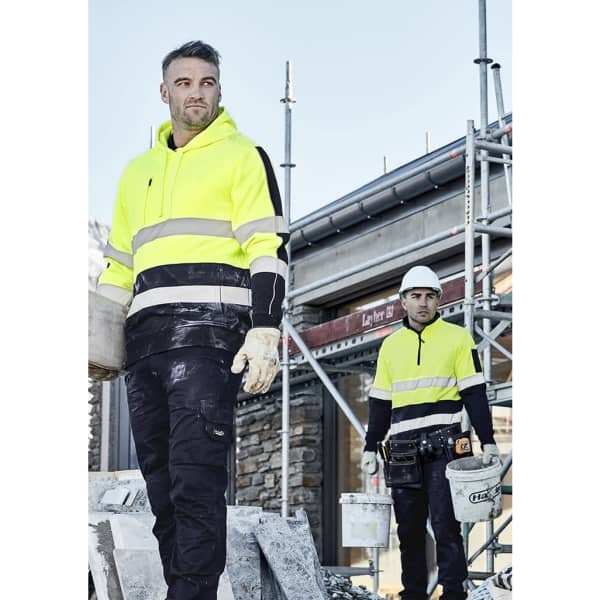 Two men wearing bright yellow hi-vis 1/4 zip pullovers with hoop tape, engaged in construction work.