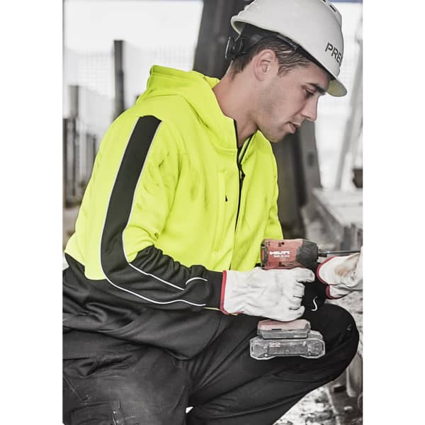 A unisex high visibility full zip hoodie in bright yellow with black accents, worn by a person holding a drill.