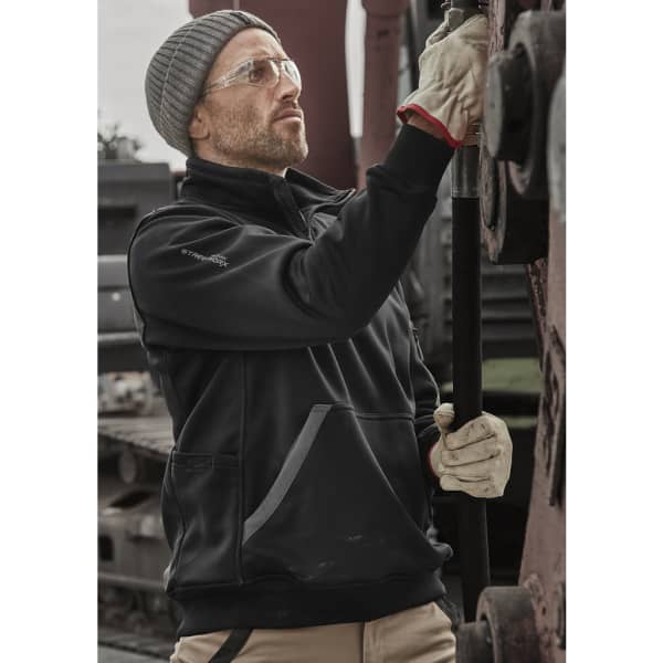 A man wearing a black unisex water-resistant pullover with a grey beanie, safety glasses, and gloves, adjusting machinery.