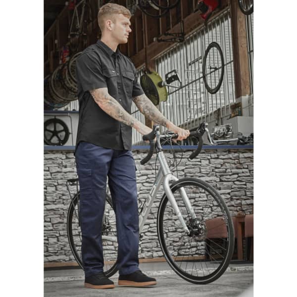 A person wearing navy midweight drill cargo pants and a black shirt stands beside a bicycle in a workshop setting.