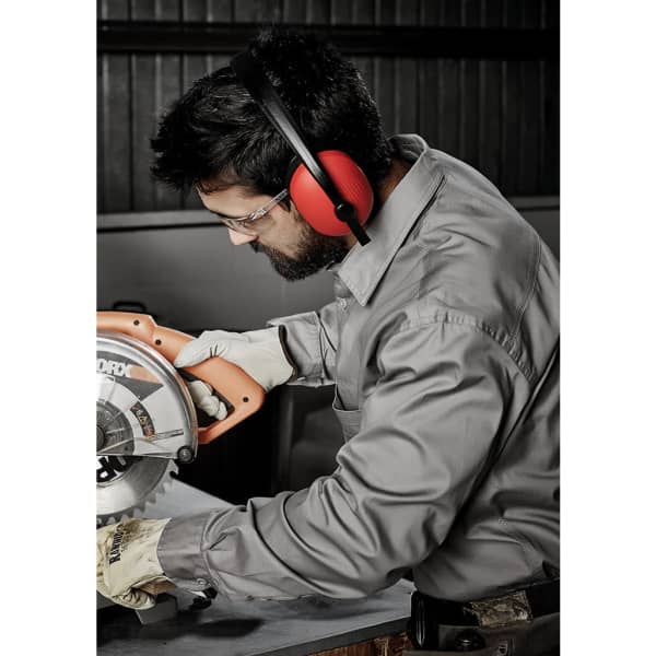 A man wearing a grey long sleeve shirt and protective gear uses a circular saw, focused on his task.