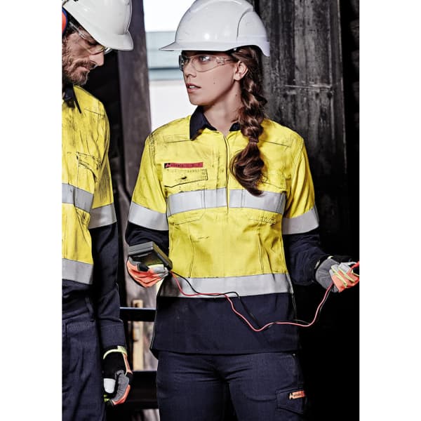 A women's yellow and navy work shirt with reflective tape and spliced design. It features a logo and is worn with safety gear.