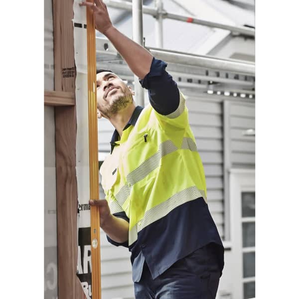 A man wearing a high-visibility segmented tape long sleeve shirt in bright yellow and navy blue, working on a construction site.