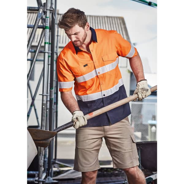 An orange and navy short sleeve shirt with reflective tape, worn by a man digging with a shovel at a construction site.