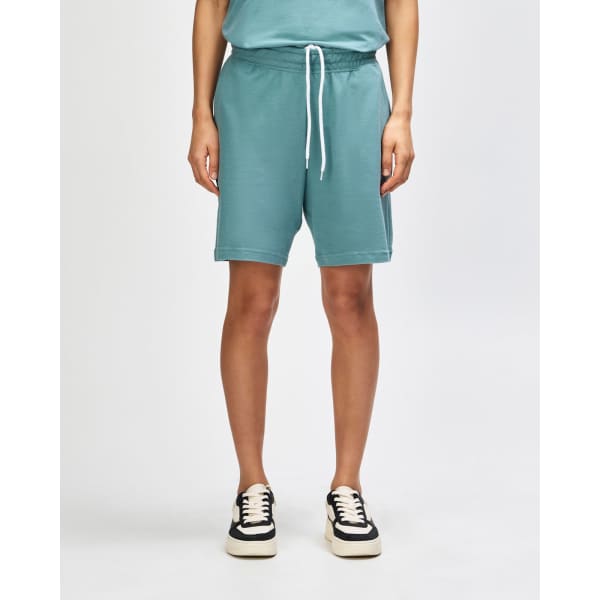 Unisex gym shorts in a soft teal colour, featuring an elastic waistband and pockets, paired with white sneakers.