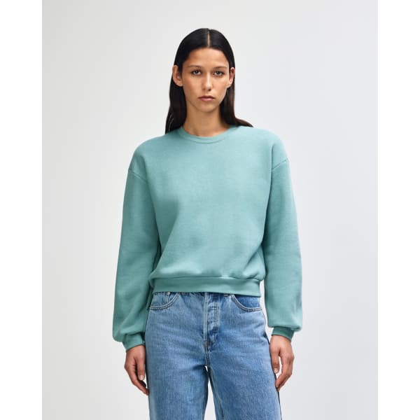 A women's crewneck sweatshirt in a soft teal colour, featuring long sleeves and a relaxed fit. It has a logo.
